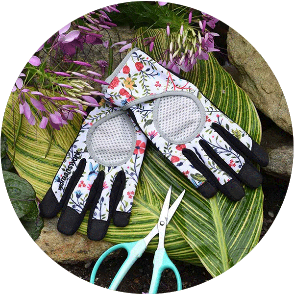 A pair of flower-print garden gloves laying on top of large green leaves, with a pair of pruners laying next to them.